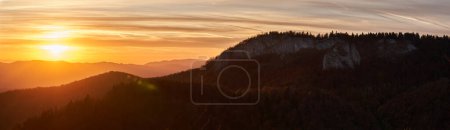Photo for Dramatic atmospheric landscape panorama with sun in frame over mountains covered in colorful autumn colored forests - Royalty Free Image