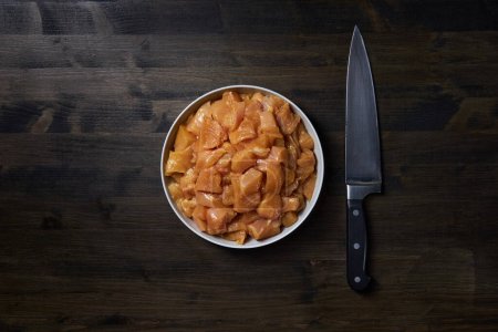 Foto de Pechuga de pollo cruda picada y un cuchillo en una tabla de madera oscura - Imagen libre de derechos