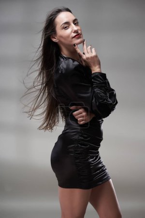 Foto de Retrato de belleza de cerca de una atractiva mujer hispana con un vestido negro ajustado, con el pelo volando sobre fondo gris - Imagen libre de derechos