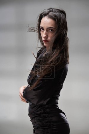 Foto de Retrato de belleza de cerca de una atractiva mujer hispana con un vestido negro ajustado, con el pelo volando sobre fondo gris - Imagen libre de derechos