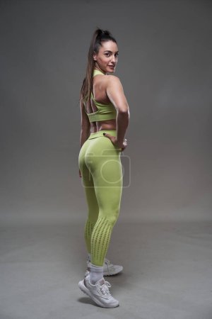 Foto de Atractiva modelo de fitness hispana posando en atuendo de gimnasio sobre fondo gris - Imagen libre de derechos