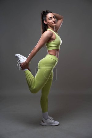 Foto de Atractiva modelo de fitness hispana posando en atuendo de gimnasio sobre fondo gris - Imagen libre de derechos