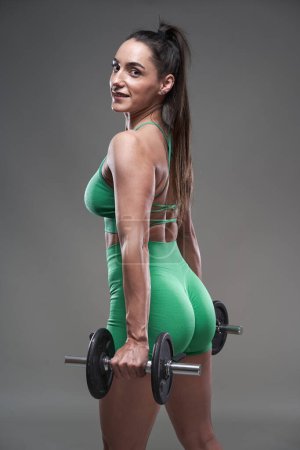 Photo for Attractive fitness model working out with dumbbells, gray background - Royalty Free Image