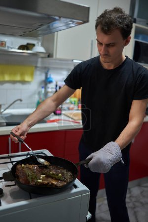 Foto de Joven preparando un bistec en una sartén de hierro fundido en una estufa de gas - Imagen libre de derechos
