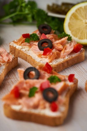 Foto de Primer plano de picaduras de filete de salmón ahumado en panes de crostini con hierbas y aceitunas, aperitivo - Imagen libre de derechos