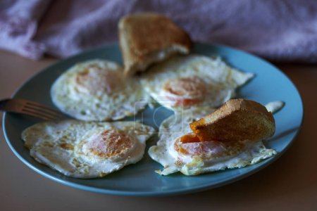 Photo for Closeup of fried eggs on a blue plate with toast digging into a yolk - Royalty Free Image
