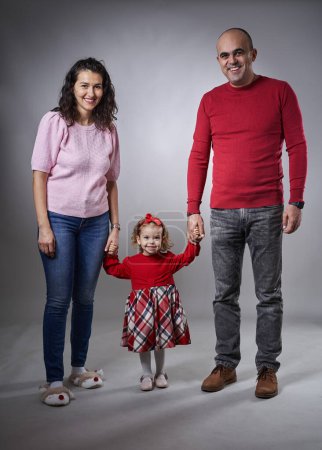 Téléchargez les photos : Joyeux jeune famille avec une jeune fille et ses parents, studio tourné sur fond gris, plan complet du corps - en image libre de droit