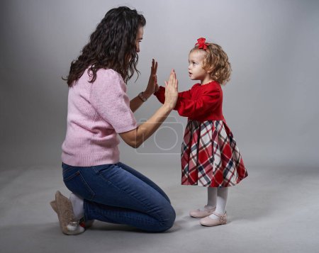 Photo for Little toddler girl playing happy with her mother, giving her high five, studio shot on gray background - Royalty Free Image