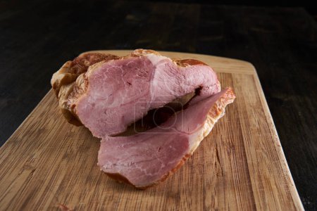 Photo for A smoked pork leg on a wooden board, sliced - Royalty Free Image