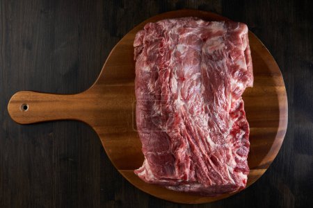 Foto de Pierna trasera de cerdo con un montón de jamón, crudo, en una tabla de cortar de madera, puesta plana - Imagen libre de derechos