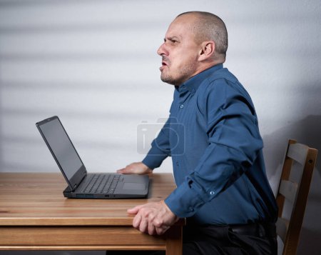 Foto de Hombre de negocios maduro sentado en su escritorio frente a su computadora portátil, hostil, enojado, amenazante - Imagen libre de derechos