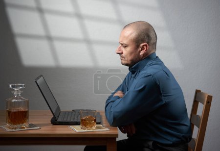Photo for Drinking at work - business man with a glass of whisky in front of his laptop - Royalty Free Image