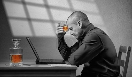 Foto de Beber en el trabajo - hombre de negocios con un vaso de whisky frente a su computadora portátil, concepto de depresión con todo menos el alcohol siendo blanco y negro - Imagen libre de derechos