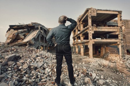 Foto de Conceptual image with a businessman holding his head looking at the ruins of a residential area, mixed media - Imagen libre de derechos