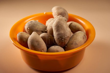 Téléchargez les photos : Une pile de pommes de terre non cuites dans un bol orange sur fond beige - en image libre de droit