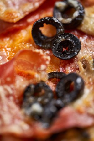 Téléchargez les photos : Macro shot sur une pizza avec du parmesan fondu couvrant des ingrédients tels que des olives, des pepperoni ou du jambon - en image libre de droit