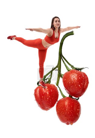 Téléchargez les photos : Concept de régime avec une femme de fitness debout en équilibre sur une énorme vigne aux tomates cerises, pleine de vitamines - en image libre de droit
