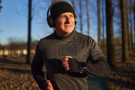 Photo for Mature athlete running in the park with headphones on, in a cold sunny winter day, closeup shot - Royalty Free Image