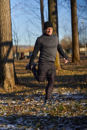 Photo for Mature runner stretching before running in a cold sunny winter day - Royalty Free Image
