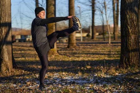 Téléchargez les photos : Coureur mature s'étirant avant de courir dans une journée froide et ensoleillée d'hiver - en image libre de droit