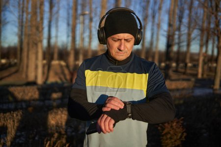 Téléchargez les photos : Runner homme mettant en place sa smartwatch avant de courir avec des écouteurs - en image libre de droit