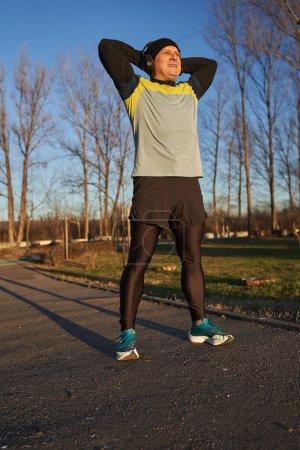 Photo for Mature recreational runner warming up and stretching before running in a cold sunny winter day - Royalty Free Image