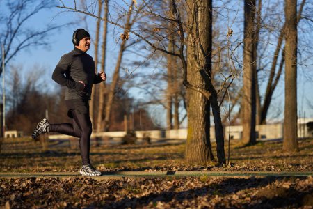 Foto de Atleta maduro con auriculares corriendo en el parque en un frío día soleado de invierno - Imagen libre de derechos