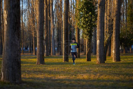 Photo for Mature athlete with headphones running in the park in a cold sunny winter day - Royalty Free Image
