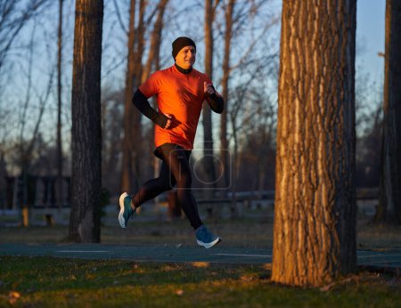 Téléchargez les photos : Homme athlétique joggin dans le parc au coucher du soleil dans une journée froide d'hiver - en image libre de droit