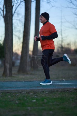 Téléchargez les photos : Homme athlétique joggin dans le parc au coucher du soleil dans une journée froide d'hiver - en image libre de droit