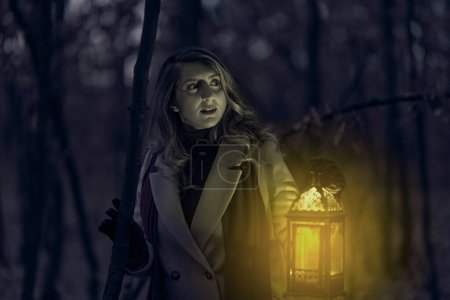 Foto de Mujer asustada por la noche en el bosque espeluznante con una linterna - Imagen libre de derechos