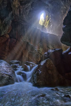 Foto de Cueva con río subterráneo y apertura en lo alto dejando pasar los rayos del sol - Imagen libre de derechos