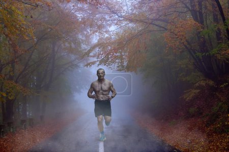 Foto de Corredor de maratón va a correr en una mañana brumosa en el bosque de montaña, en un camino cubierto de neblina ondulada - Imagen libre de derechos