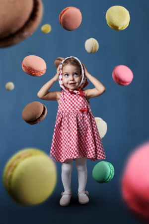 Téléchargez les photos : Bonne petite fille entourée d'une pluie de macarons volants, plan conceptuel d'avoir une dent sucrée, art numérique mixte - en image libre de droit