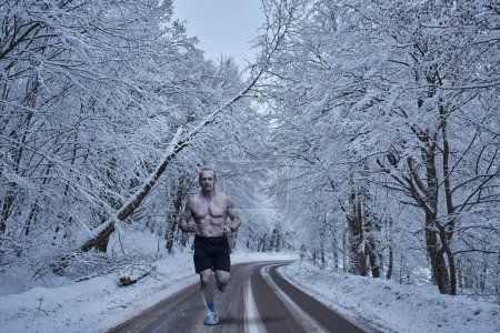 Foto de Corredor de maratón en invierno, corriendo sin camisa en una carretera congelada en una fría mañana - Imagen libre de derechos