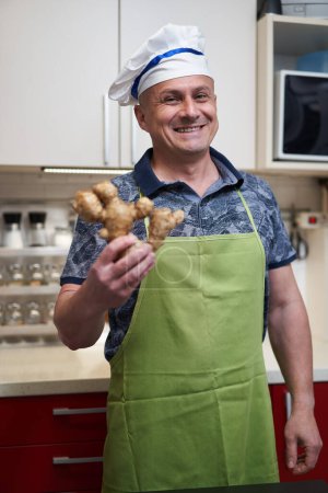 Téléchargez les photos : Homme cuisinier dans la cuisine tenant un grand morceau de gingembre - en image libre de droit