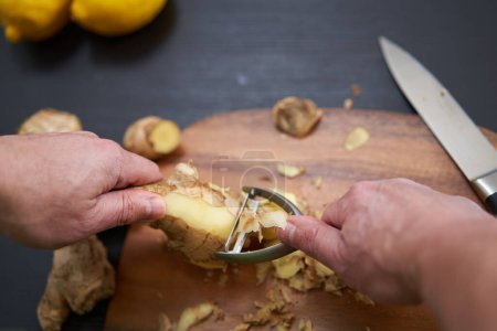 Photo for Man cook peeling and cleaning a large ginger root on a wooden board - Royalty Free Image