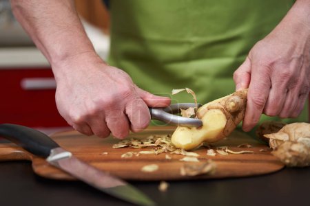 Man cook peeling and cleaning a large ginger root on a wooden board