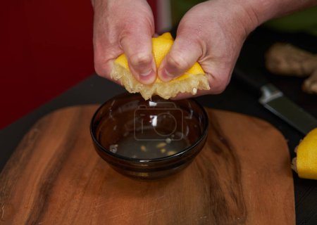 Photo for Man cook squeezing half a lemon into a bowl on a wooden board - Royalty Free Image