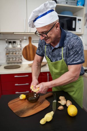 Téléchargez les photos : Homme cuisinier pressant dur la moitié d'un citron dans un bol en verre sur une planche en bois - en image libre de droit