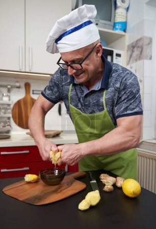 Photo for Man cook squeezing hard half a lemon into a glass bowl on a wooden board - Royalty Free Image