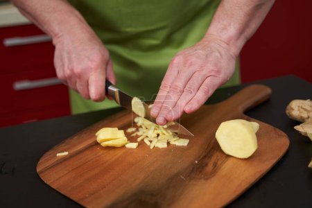 Photo for Man chef chopping ginger finely on a wooden board with a very sharp knife - Royalty Free Image