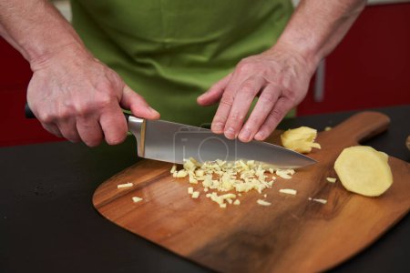 Téléchargez les photos : Homme chef hacher du gingembre finement sur une planche de bois avec un couteau très pointu - en image libre de droit