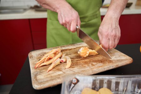 Téléchargez les photos : Homme cuisinier enlever les pointes des ailes de poulet et les couper en deux pour une recette - en image libre de droit