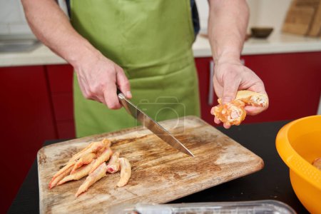 Téléchargez les photos : Homme cuisinier enlever les pointes des ailes de poulet et les couper en deux pour une recette - en image libre de droit