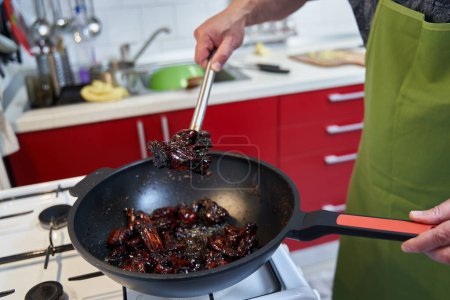 Téléchargez les photos : Gros plan de l'homme cuisinant des ailes de poulet caramélisées dans un wok, une recette de spécialité thaï - en image libre de droit