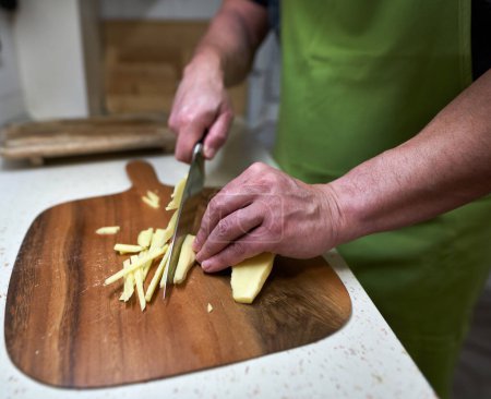 Téléchargez les photos : Chef masculin hachant du gingembre sur une planche de bois rustique dans la cuisine - en image libre de droit