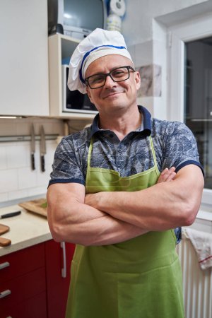 Photo for Man in apron and cap as a cook at home, in the kitchen - Royalty Free Image
