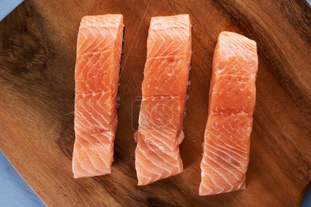 Foto de Filetes de salmón crudo en una tabla de madera, listos para asar - Imagen libre de derechos