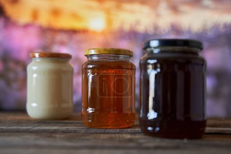 Téléchargez les photos : Différents types de miel dans des pots sur une planche en bois dans une belle vue sur la montagne avec des fleurs - en image libre de droit